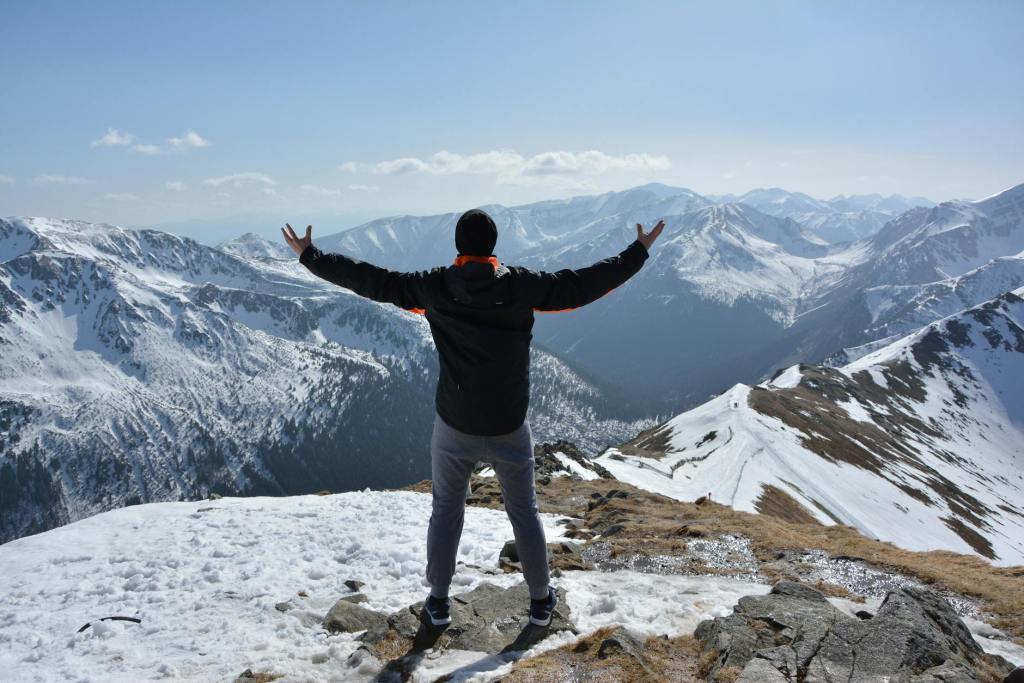 A man stands triumphantly atop a snowy mountain. He feels like he's conquered the world!