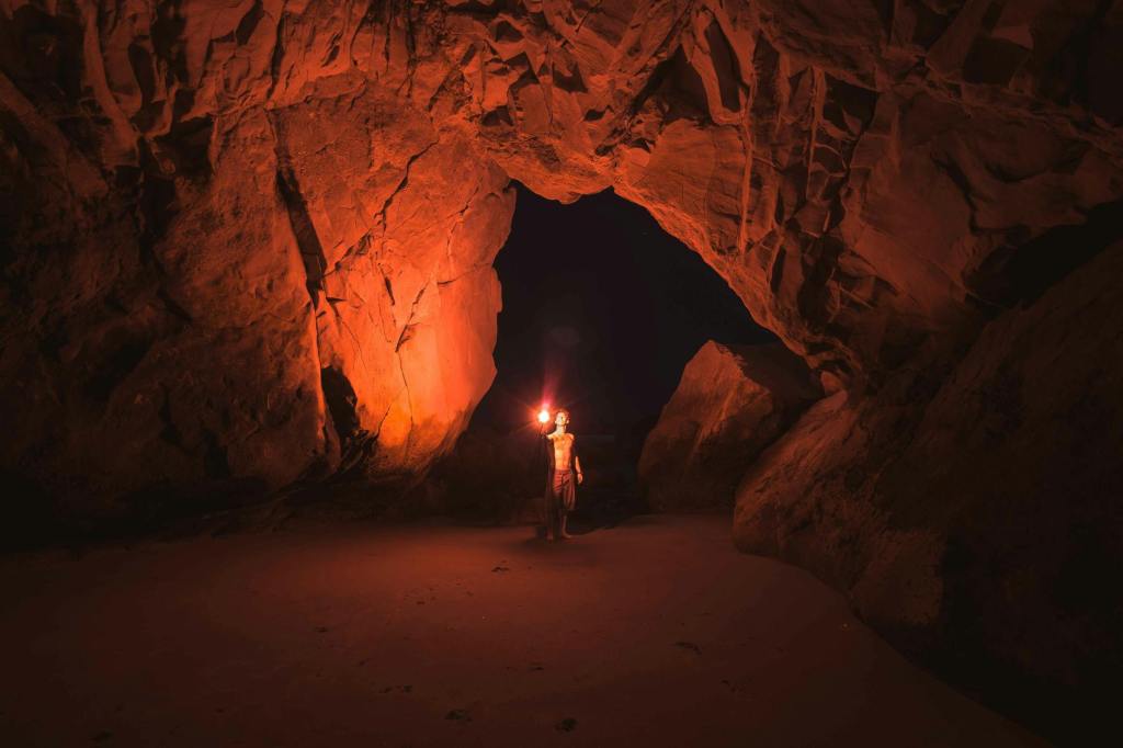 A man stands alone in a cave. The only light source is the torch he holds above his head. He looks up in awe.
